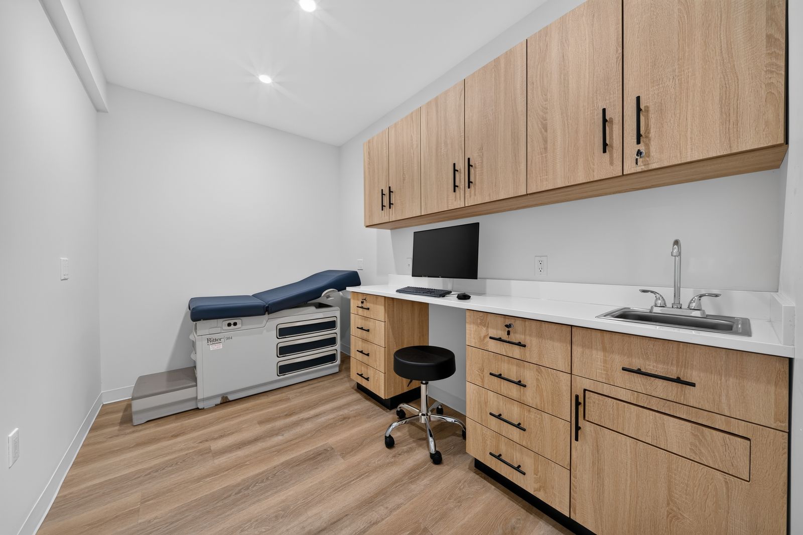 Exam room with a Ritter exam table, wood cabinets, a sink and a computer workstation